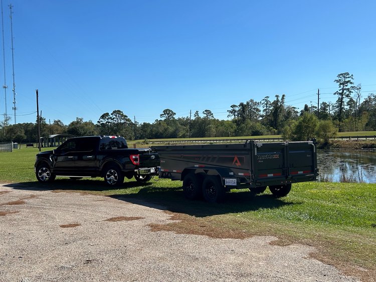 RawMaxx dump trailer parked by a pond, towed by a Ford F-150.