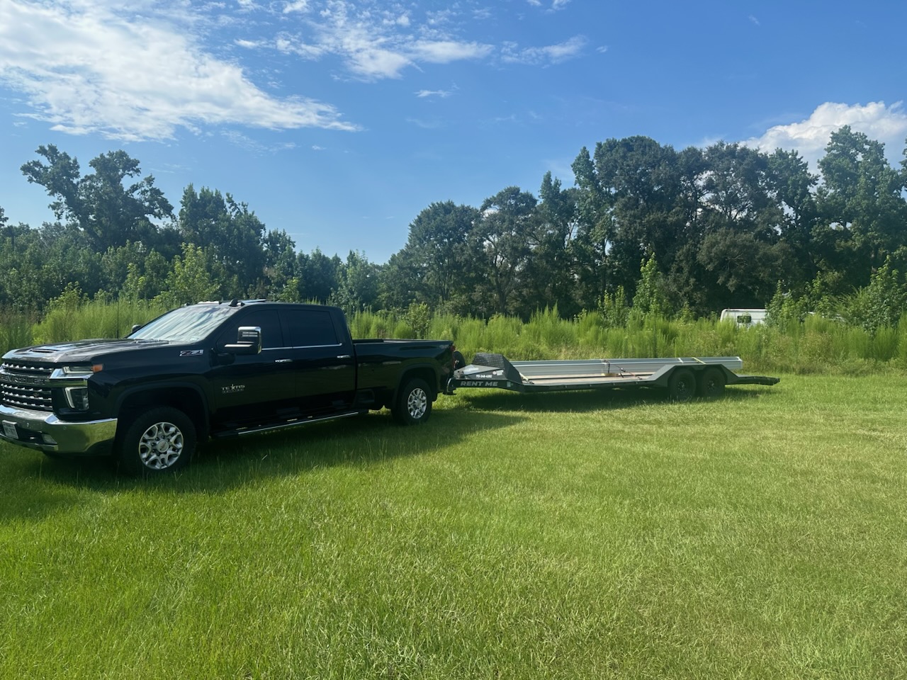 Black pickup truck with an empty flatbed trailer in a grassy field.